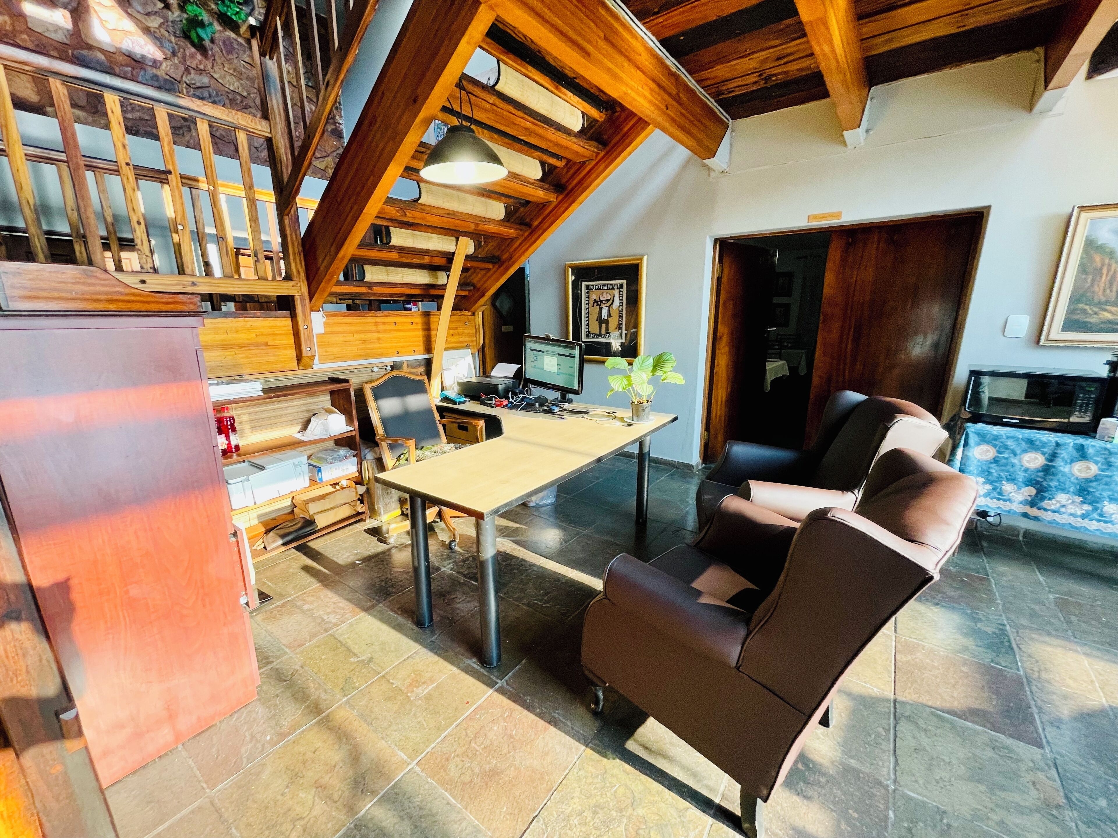 Amplia sala de estar con techo alto, vigas de madera, una mesa de comedor, un sofá y una zona de cocina con microondas.