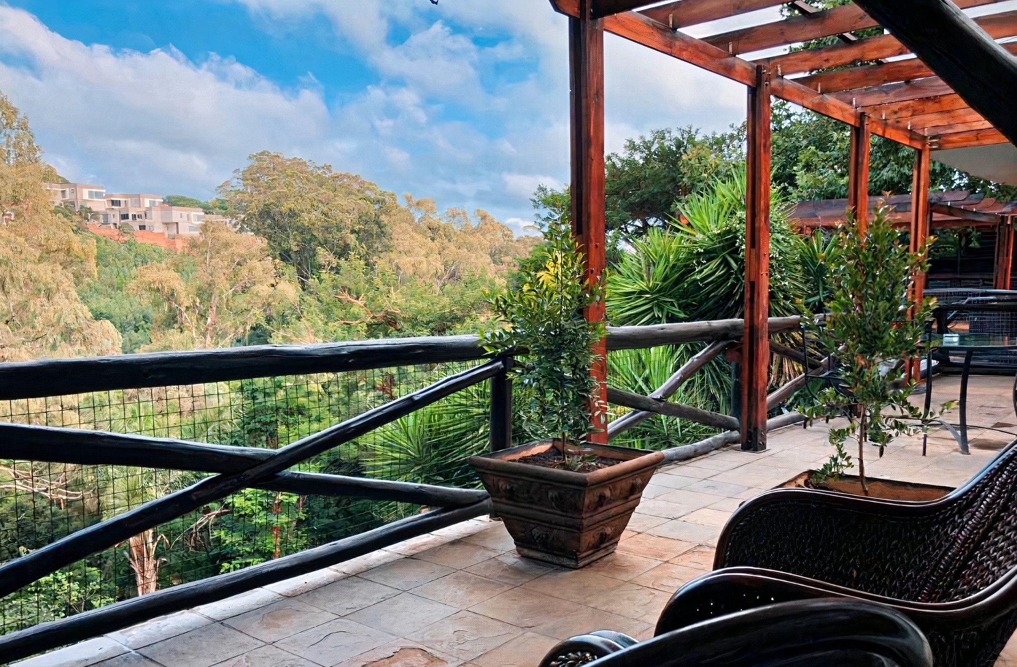 A balcony with a wooden pergola, potted plants, and a view of a hilly landscape.