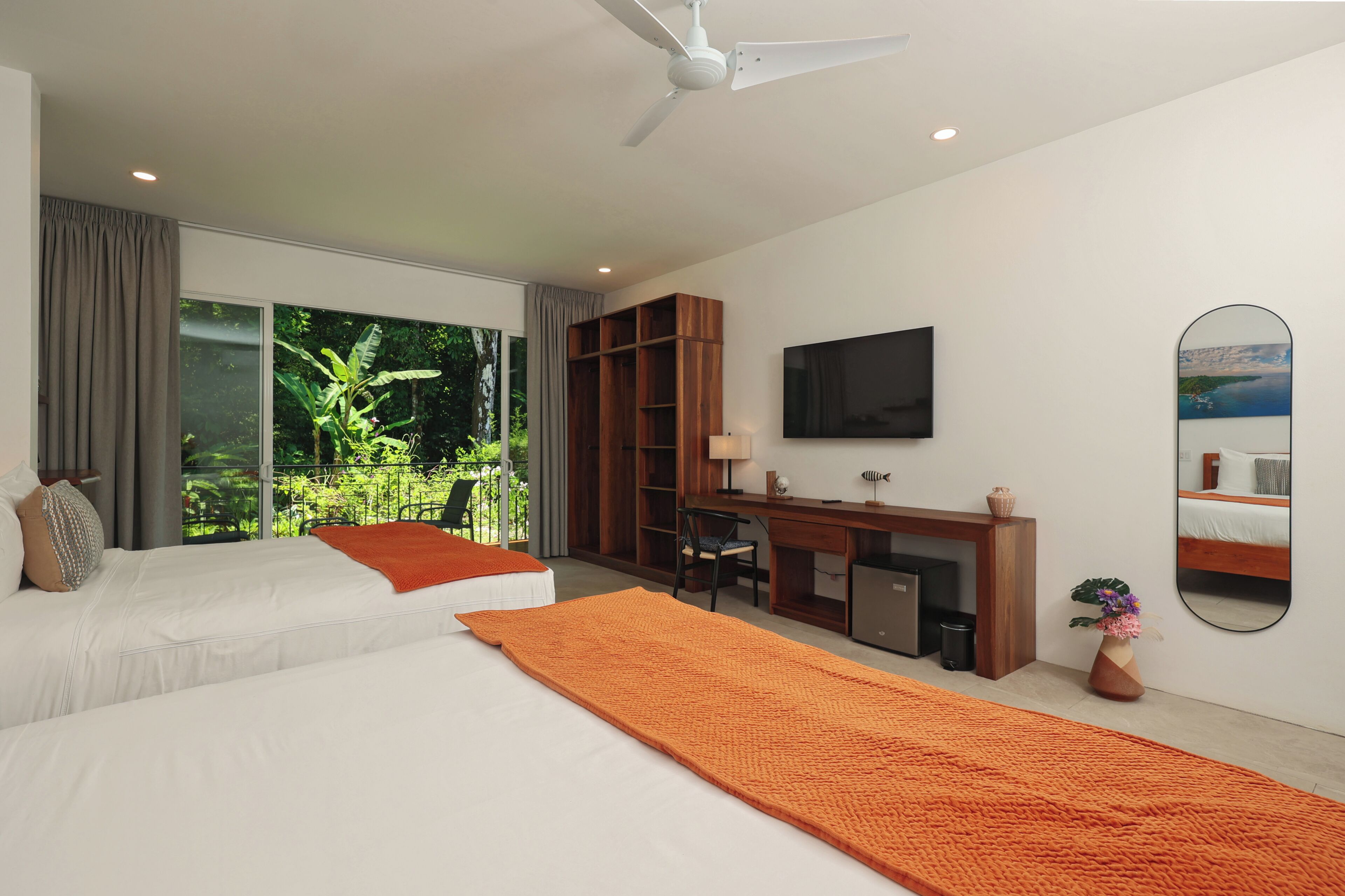 A modern hotel room with two beds, a desk, a television, and a large window with a view of greenery.