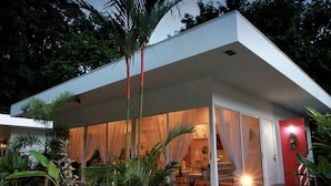 Een modern huis met een overdekte veranda, een rode deur en een verzorgde tuin.