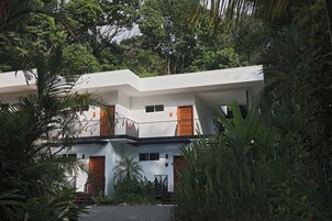 Un edificio moderno de dos pisos con balcones, rodeado de exuberante follaje.
