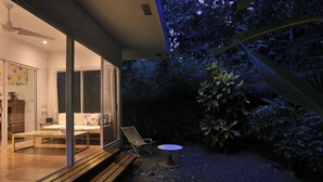 Een modern huis met een patio met glazen wanden, een houten terras en een kleine ronde tafel.
