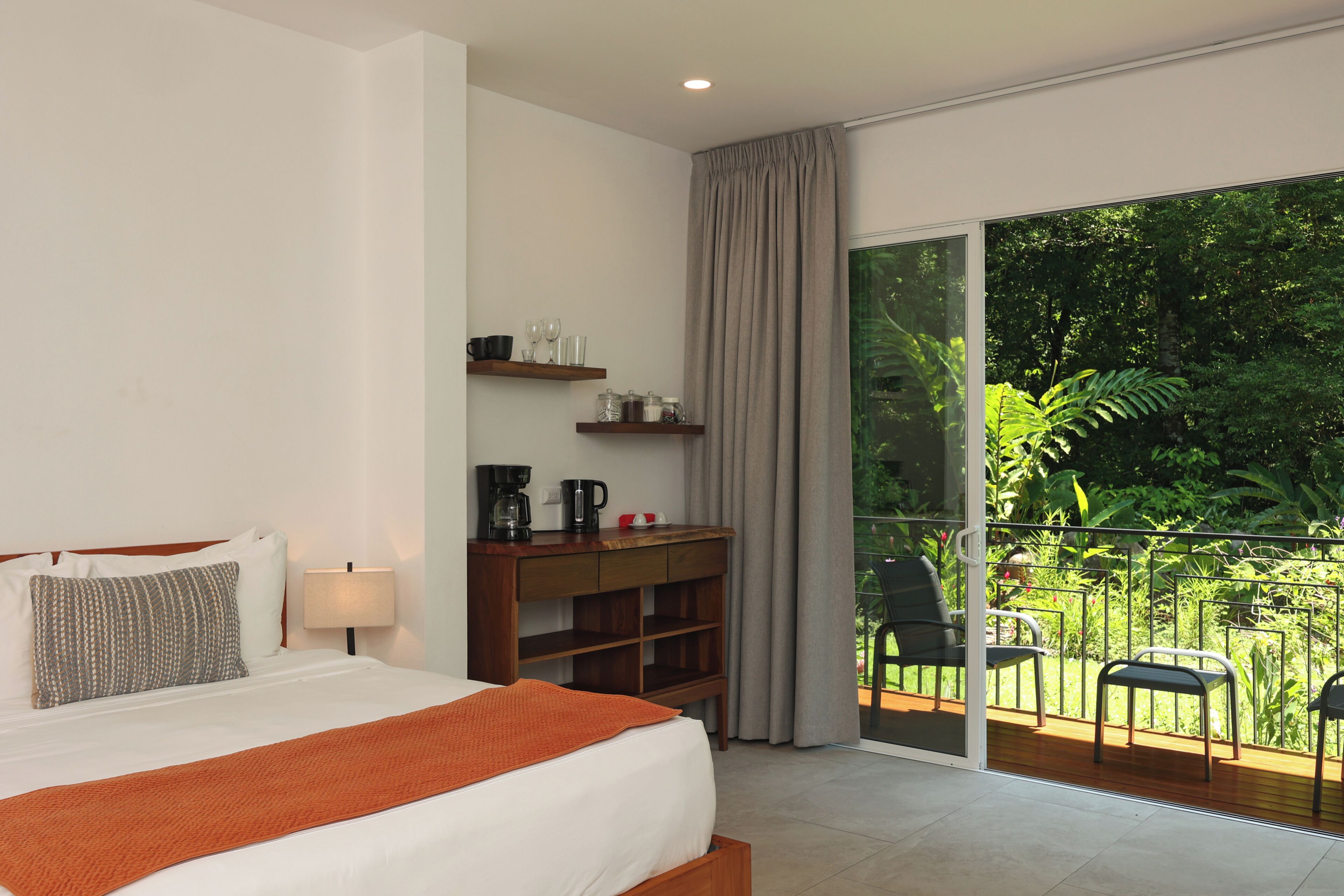 Une chambre d’hôtel avec un lit, un bureau doté d’une machine à café, une vue sur un balcon avec des chaises et une grande fenêtre.