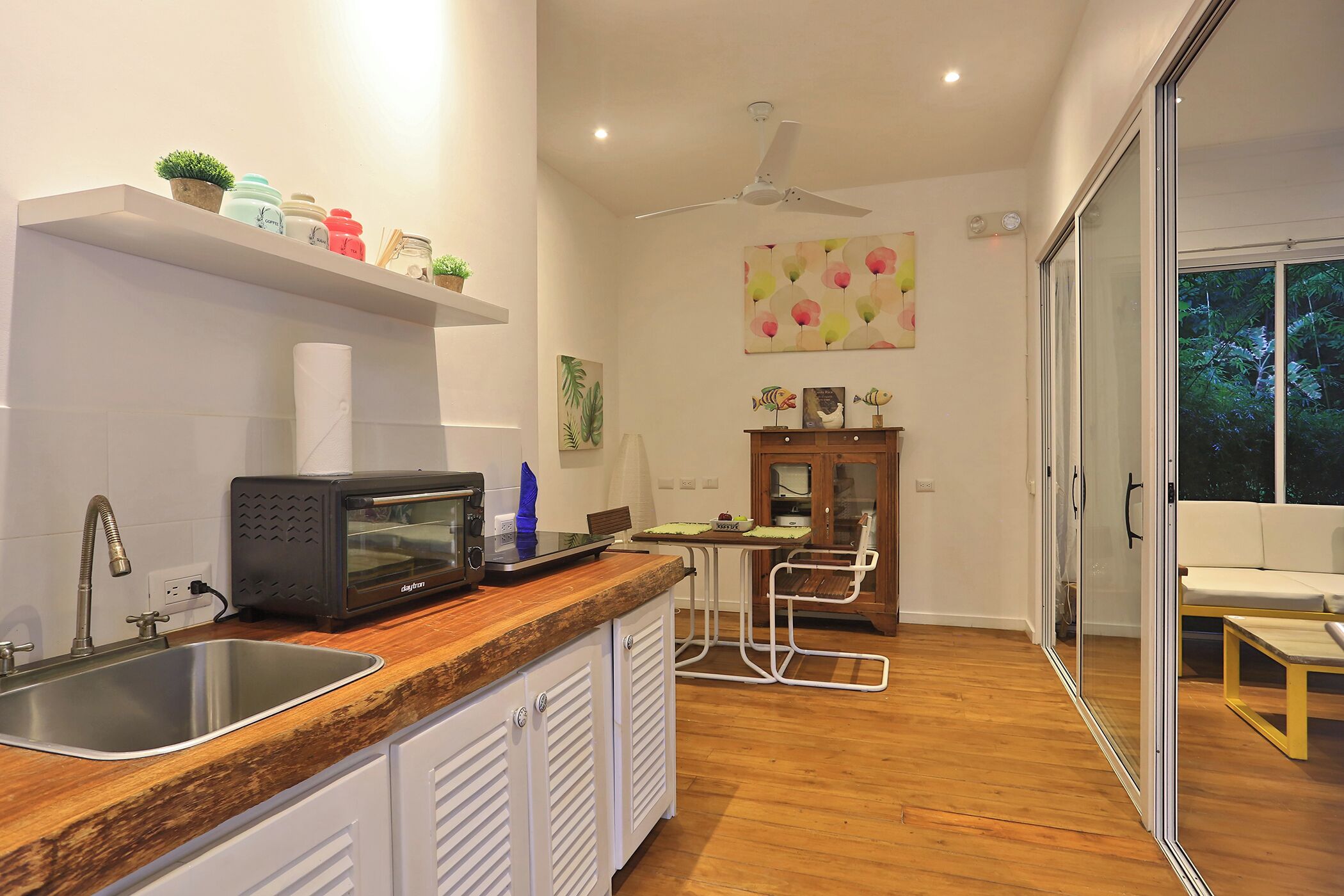 Een moderne keuken met een ingebouwde magnetron, een spoelbak en een houten aanrechtblad. Er is een eethoek met een tafel en stoelen, en een schuifpui die uitkomt op een balkon.