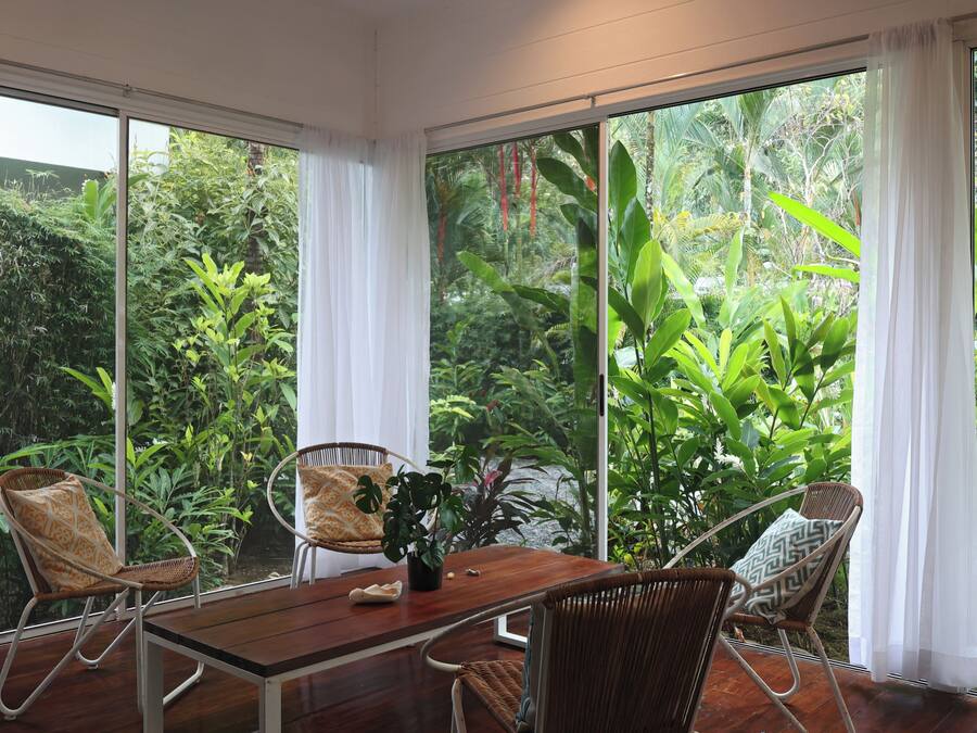Una habitación con una mesa de madera, dos sillas de mimbre y vistas a la vegetación exuberante a través de amplios ventanales.