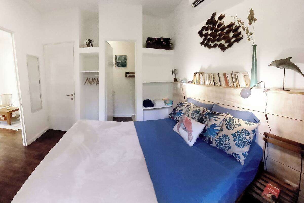 Un dormitorio con cama, mesitas de noche, lámpara, estantería y un adorno en la pared.