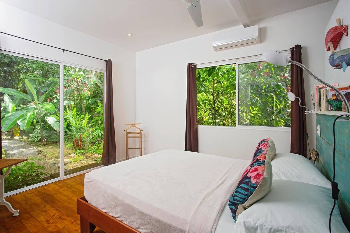 Un dormitorio con cama, escritorio y ventana con vistas a un jardín.