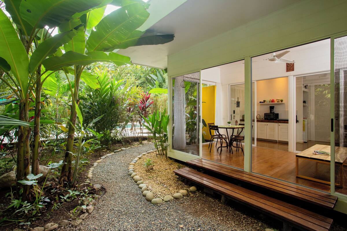Una casa moderna con un patio, un comedor y una cocina visibles a través de puertas de vidrio.