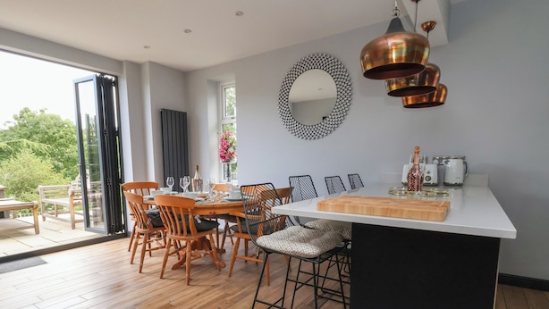 A modern kitchen with a central island, wooden dining chairs, and a large window. - Bryn Gwynedd (Conwy)