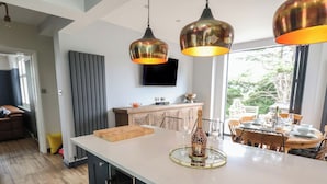 A modern kitchen with a large island, pendant lighting, and a dining area with a view. - Bryn Gwynedd (Conwy)