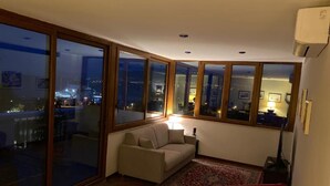 A living room with a large sliding glass door, a sofa, a red chair, and a patterned rug. - Casa Malù----------- (Messina)