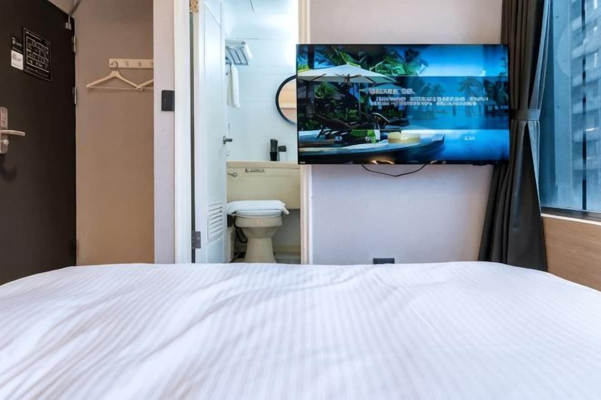 A hotel room with a bed, a television mounted on the wall, a toilet, and a sink.