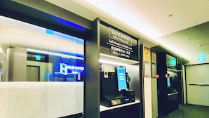 Ein Selbstbedienungsschalter mit einem digitalen Kiosk, einem Schild mit der Aufschrift „24-Stunden-Service“ und im Hintergrund der HUB HOTEL.