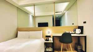 Ein Hotelzimmer mit einem Bett, einem Schreibtisch, einem Stuhl, einem Spiegel und einem kleinen Tisch mit Telefon und Kaffeemaschine.