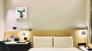 Ein Hotelzimmer mit einem Bett, einem Schreibtisch mit Stuhl, einem Wandbild und einem Nachttisch mit Lampe und Telefon.