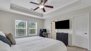 Une chambre à coucher avec un grand lit, un ventilateur de plafond, une télévision et une commode.