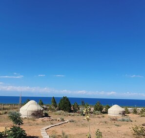 Two yurts in a dry, grassy area with a clear blue sky and a body of water in the background.