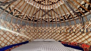 A yurt interior with a bed, a circular wooden ceiling, and a lattice wall. - Agat Yurt Camp (Kaji-Say)
