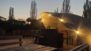 An outdoor seating area with tables and benches, a covered structure, and trees in the background. - Agat Yurt Camp (Kaji-Say)