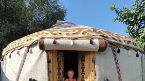 A yurt with a child standing at the entrance, a patterned rug, and a pair of shoes on the ground. - Agat Yurt Camp (Kaji-Say)