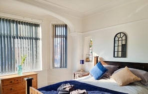 Classic bedroom with a large bed, dresser, and window with vertical blinds.