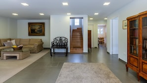 Een ruime woonkamer met een bank, een bijzettafeltje, een boekenkast en een trap naar een andere kamer.