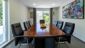 Een vergaderruimte met een lange tafel, zes stoelen en een schilderij aan de muur.