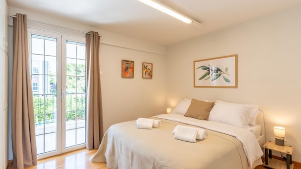 Een slaapkamer met een groot bed, een nachtkastje met een lamp en uitzicht op groen buiten het raam.