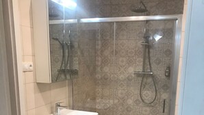 Ein modernes Badezimmer mit einer gläsernen Duschkabine, einem weißen Waschbecken mit Holzschubladen und Wandfliesen mit Muster.
