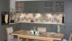 Eine Küche mit grauen Schränken, einem Holztisch und einer gemusterten Spritzschutzwand.