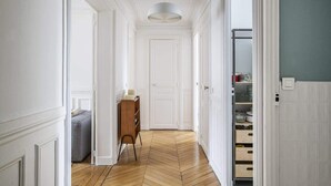 A hallway with a herringbone floor, white walls, a wooden cabinet, and a grey sofa.