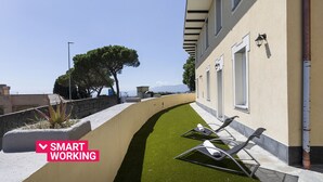 Un edificio moderno con un sendero curvo, mobiliario exterior y vistas al mar.