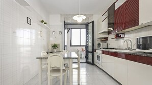 A modern kitchen with white cabinetry, a dining area with white chairs, and a large window providing natural light. - Casa Giovanna by Wonderful Italy (Bari)