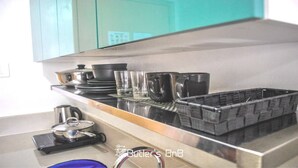 A kitchen with a stainless steel countertop, a coffee maker, and a basket of utensils. - Room-butler's Bnb B Trees Residences Qc (Quezon City)