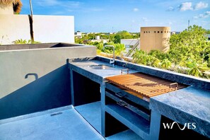 A rooftop bar with a built-in grill, a sink, and a view of the cityscape.