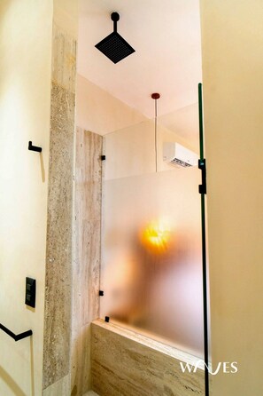 Un baño moderno con ducha, paredes de mármol y una lámpara en el techo.