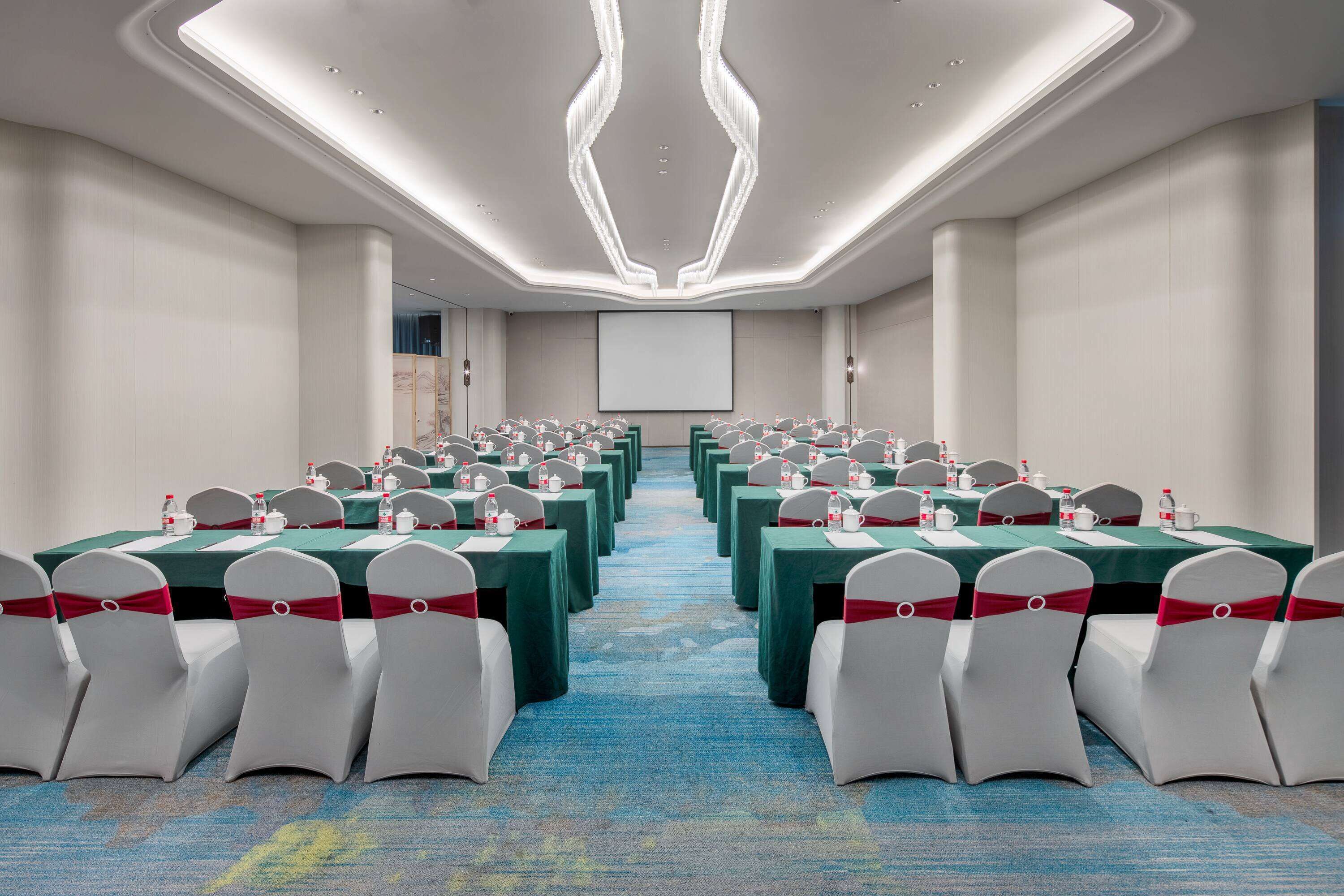 A conference room with rows of tables and chairs, equipped with water bottles and tea sets.