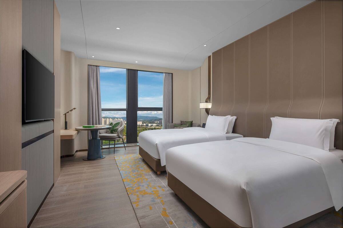 A hotel room with two beds, a TV, a balcony with a view, and a small table with chairs.