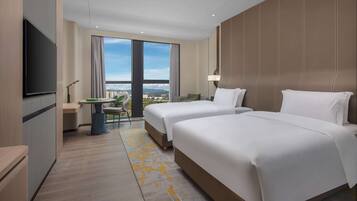 A hotel room with two beds, a TV, a balcony with a view, and a small table with chairs.