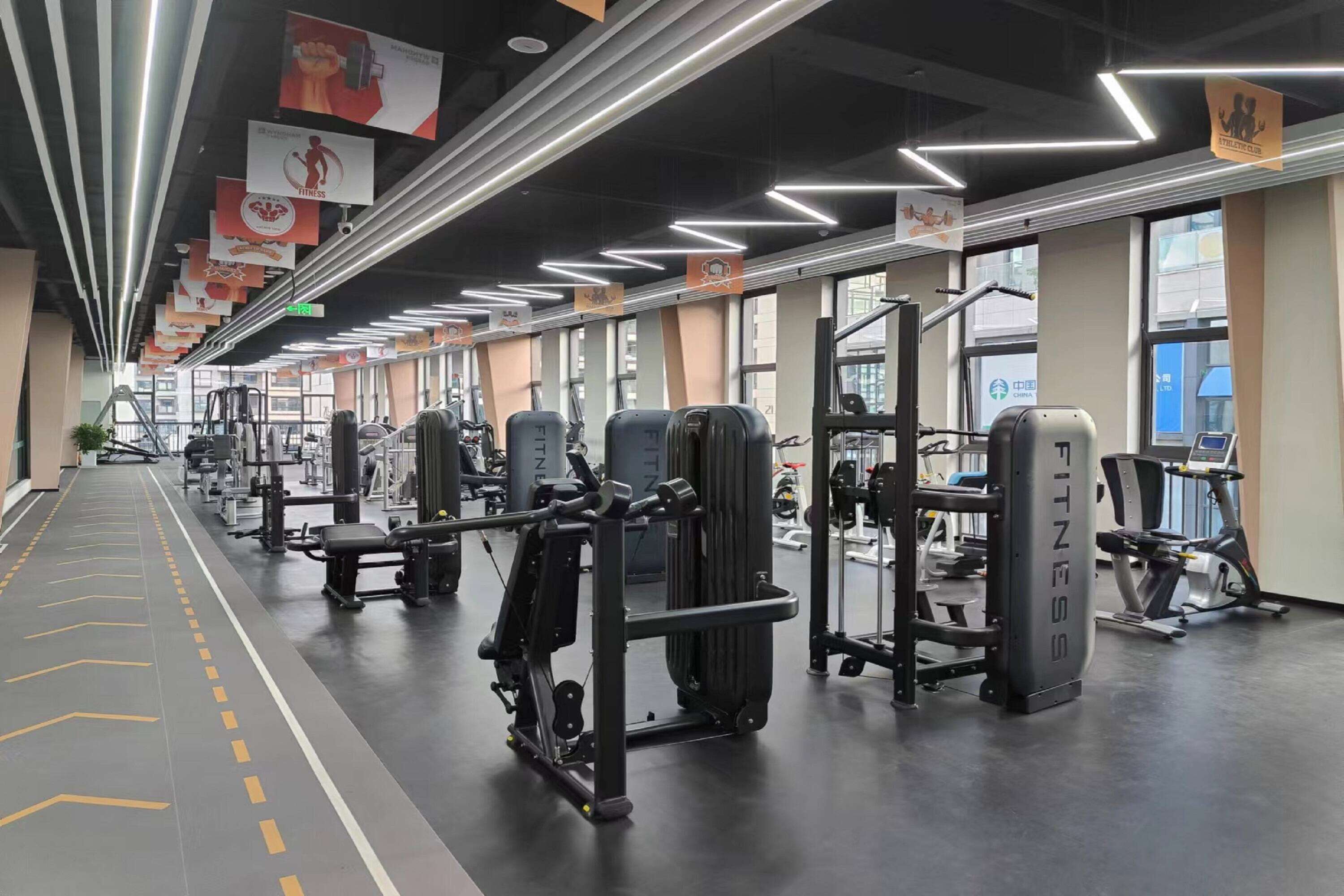 A gym with various exercise machines, a clear path for walking, and large windows allowing natural light.