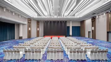 A large conference room with rows of white chairs, a stage, and a blue carpet.