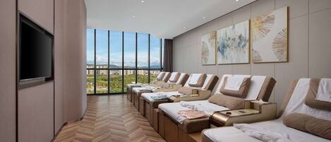 Un spa moderno con varias camillas de masaje, un televisor de pantalla plana y grandes ventanales con vistas a la ciudad.