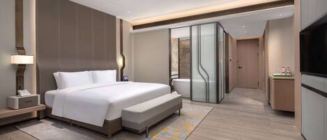 Una habitación de hotel moderna con una cama grande, mesita de noche, lámpara y baño con bañera y ducha.