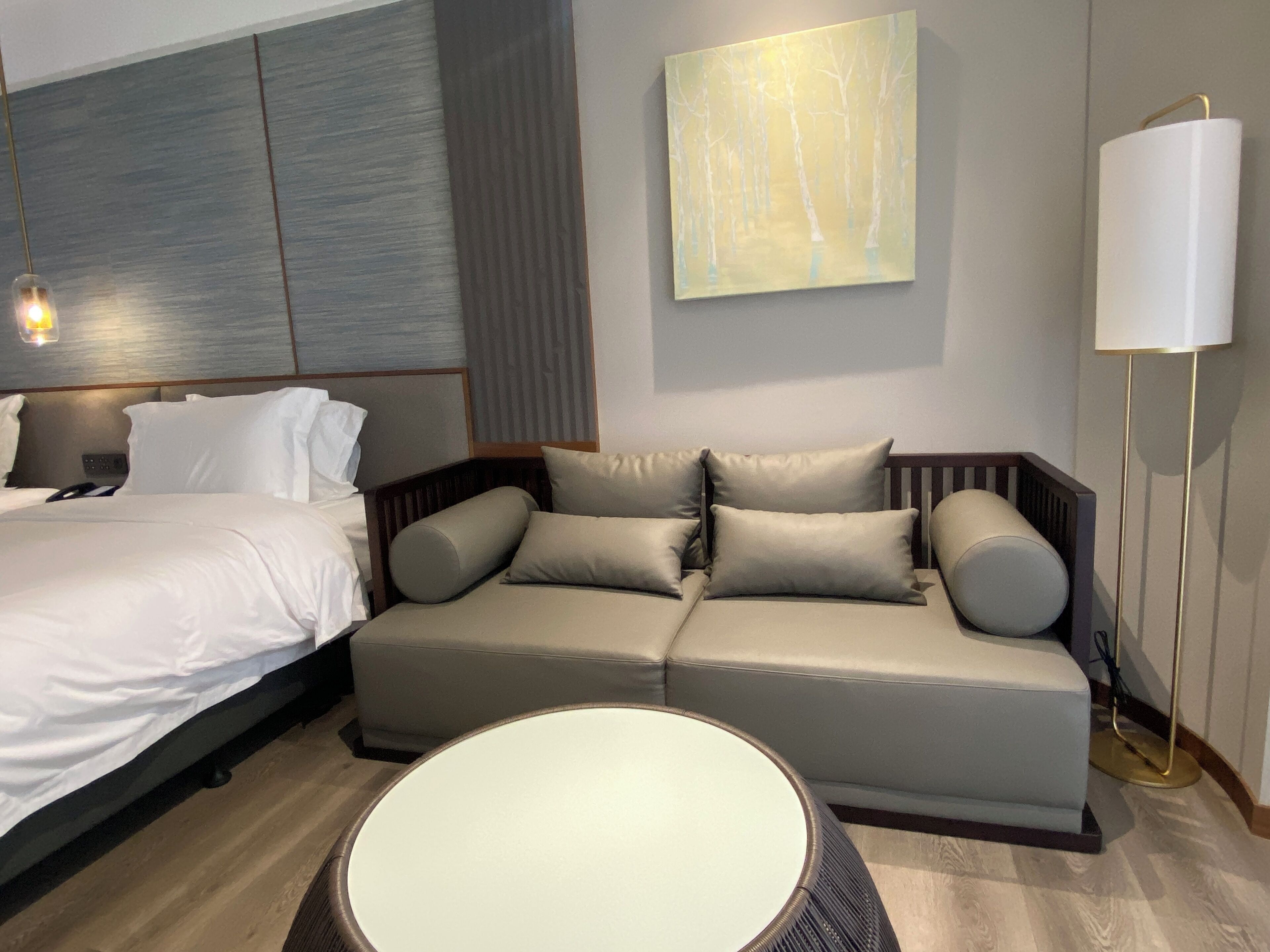 Ein modernes Hotelzimmer mit Bett, Sofa, rundem Tisch und Stehlampe.