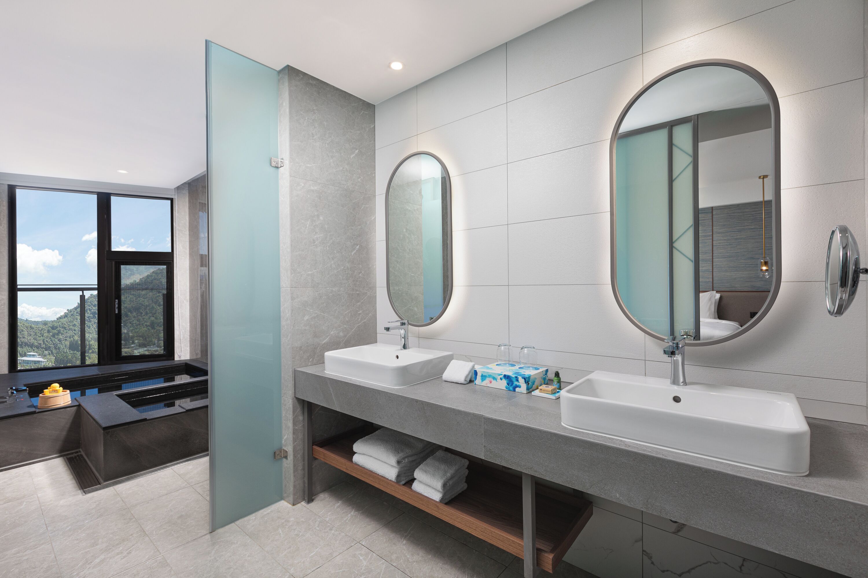 A modern bathroom with two sinks, large mirrors, and a view of the outdoors.