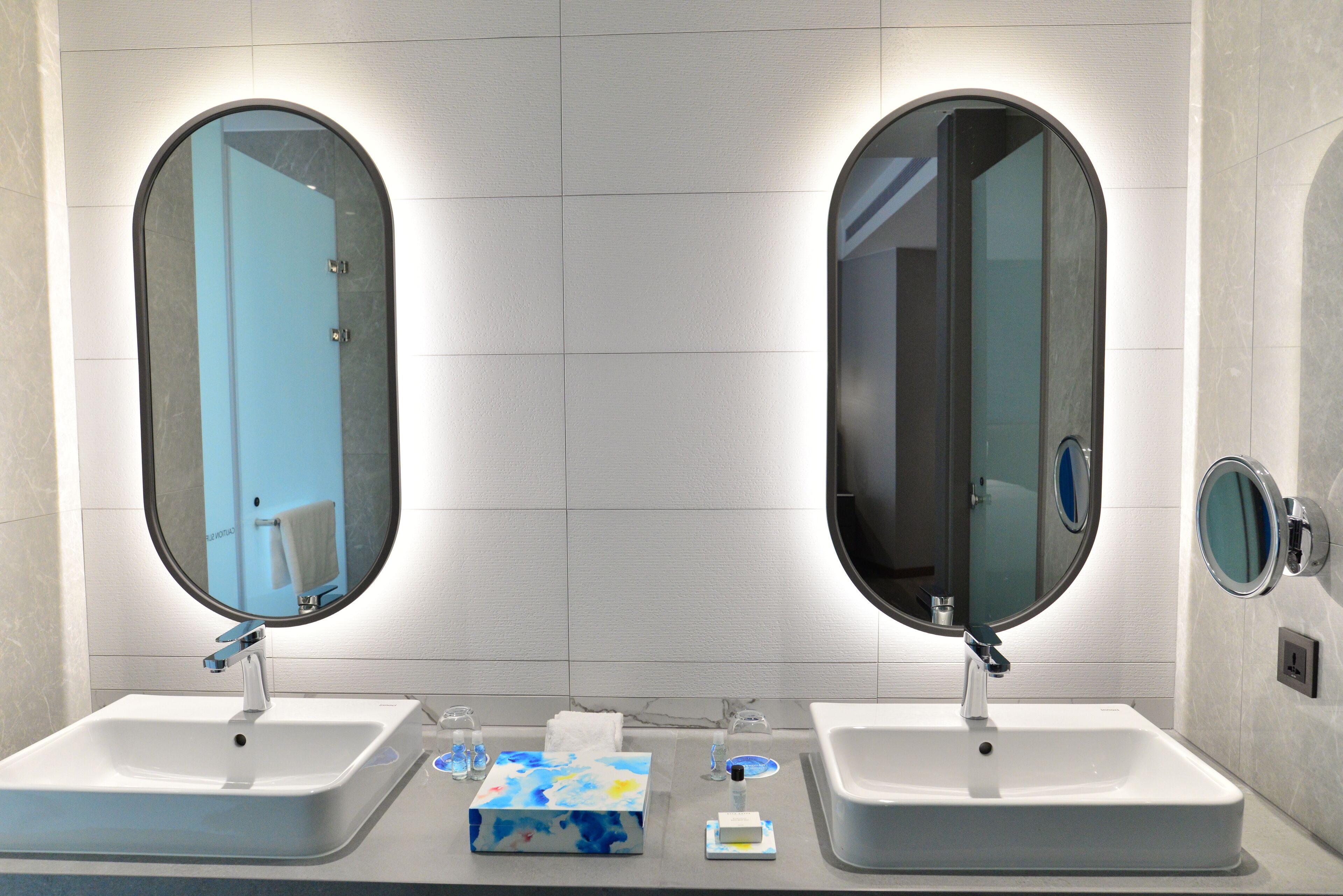 A bathroom with two sinks, each with a mirror and a faucet. There are toiletries on the counter.