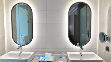 Un baño con dos lavamanos, cada uno con espejo y grifo. Hay artículos de aseo en la encimera.