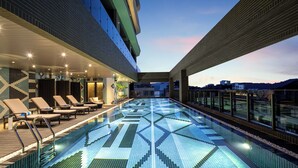 A rooftop swimming pool with a geometric tile pattern, lounge chairs, and a view of the city skyline. - Wyndham Sun Moon Lake (Yuchi)