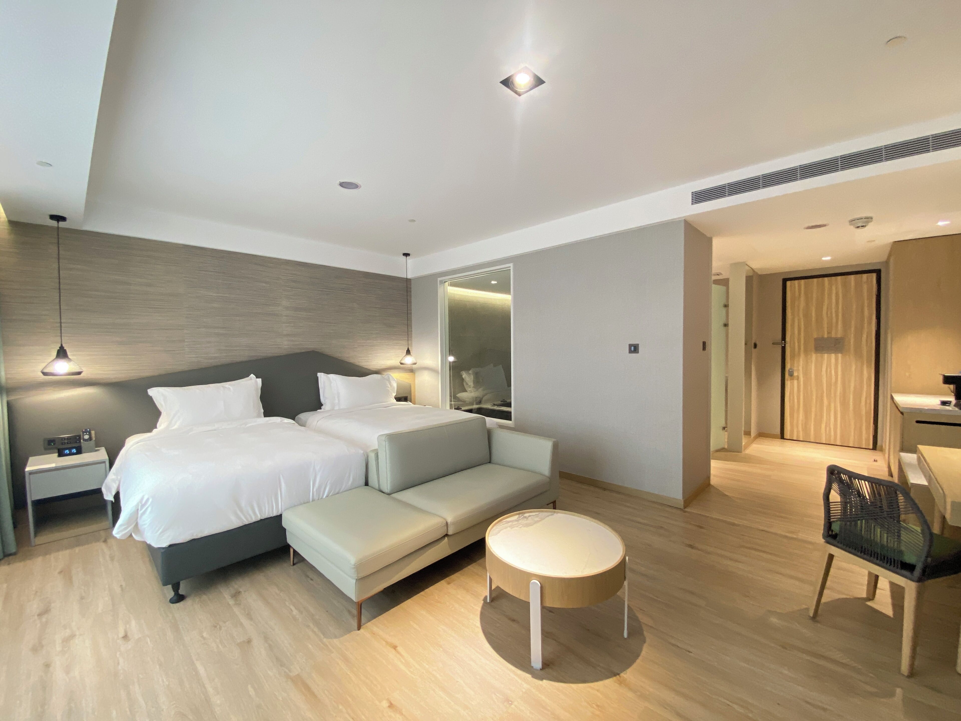 A modern hotel room with a large bed, a sofa, a round wooden table, and a chair.