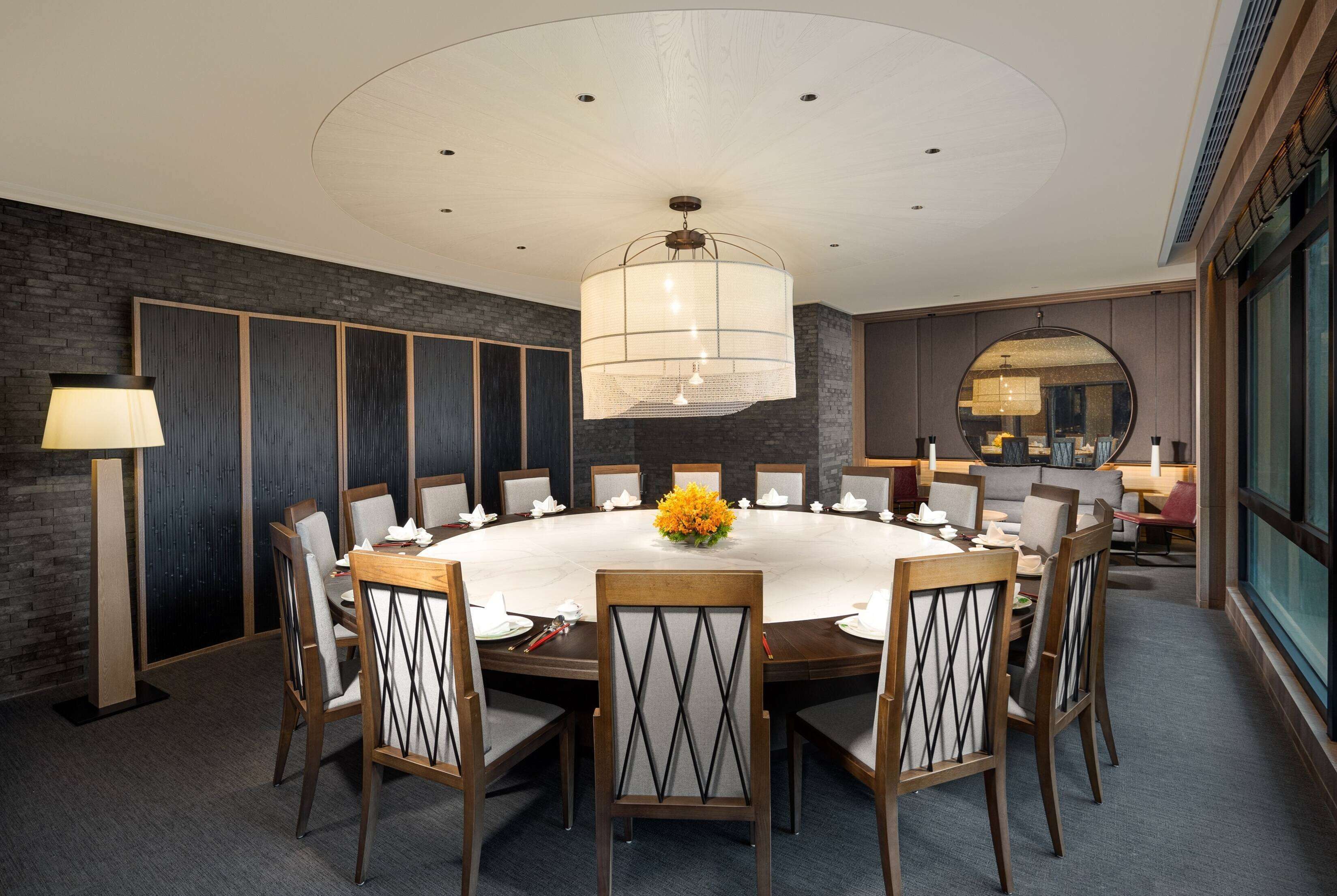 A conference room with a round table, chairs, a chandelier, and a large mirror.